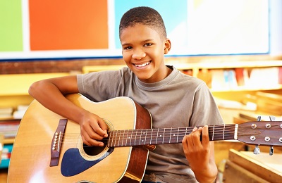 child with a smile holding a
        guitar